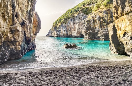 Ukrytá pláž mezi skalami s průzračnou vodou.