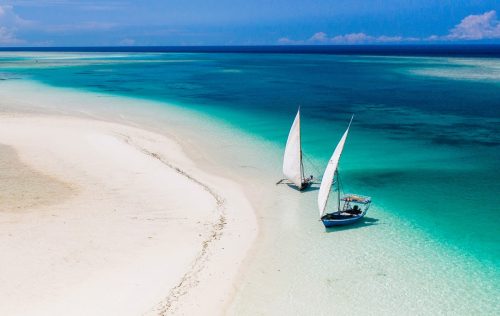 Krásná bílá pláž se dvěma kotvícími plachetnicemi a modrým mořem na ostrově Zanzibar