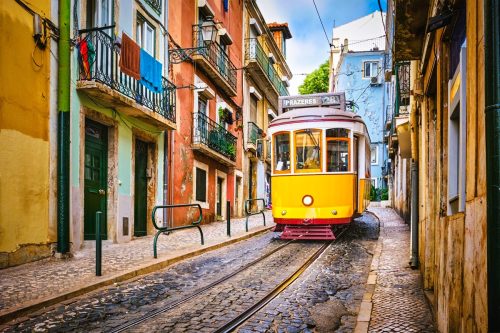Historická žlutá tramvaj projíždí úzkou ulicí v centru Lisabonu.