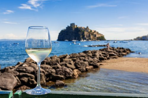 Sklenka bílého vína s výhledem na Aragonský hrad a moře na ostrově Ischia.
