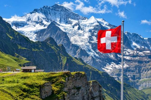 Švýcarská vlajka na pozadí majestátních vrcholů Bernských Alp v oblasti Jungfrau.